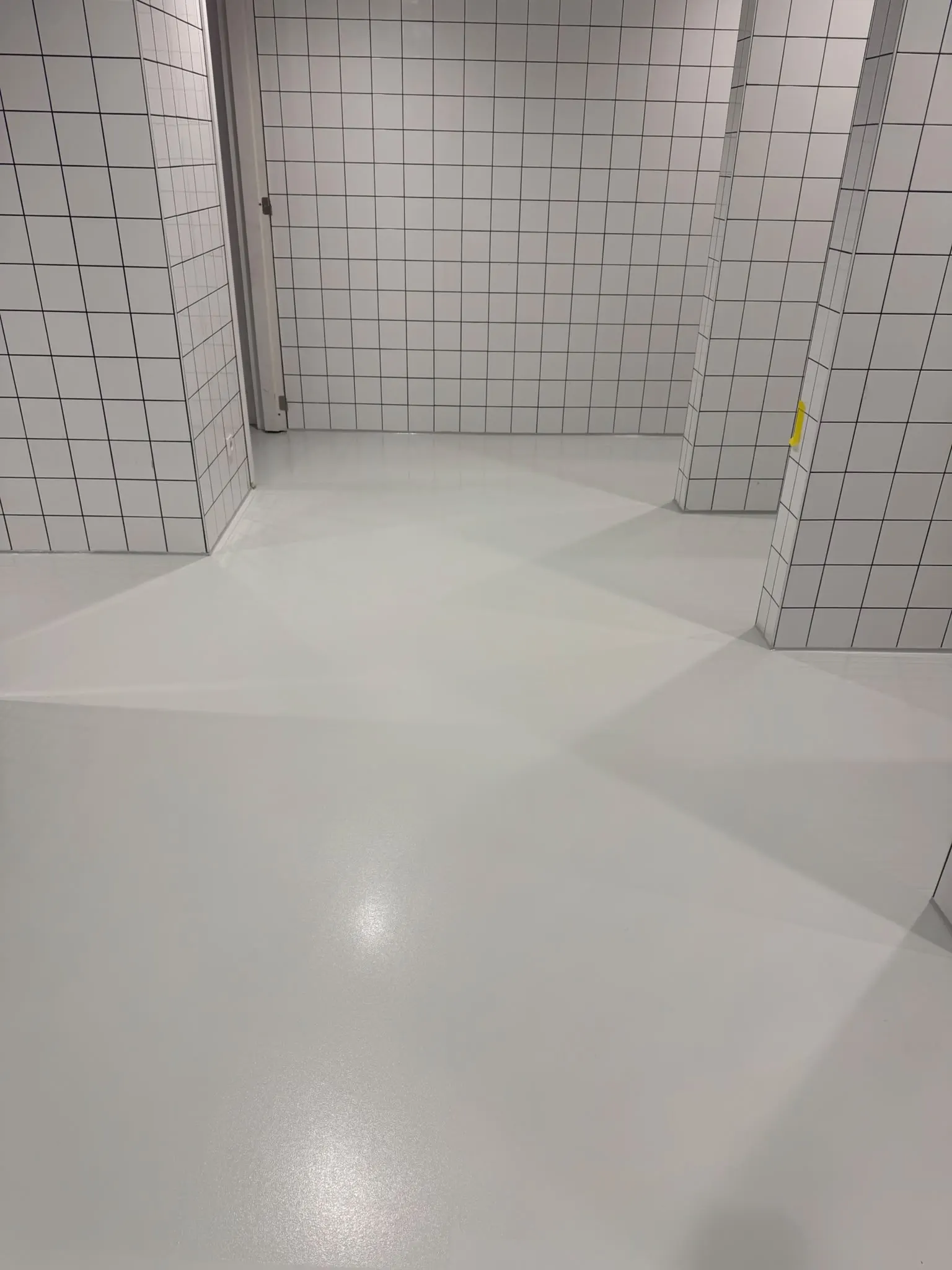 Ruimte met witte tegelwanden en een lichtgrijze, glanzende vloer